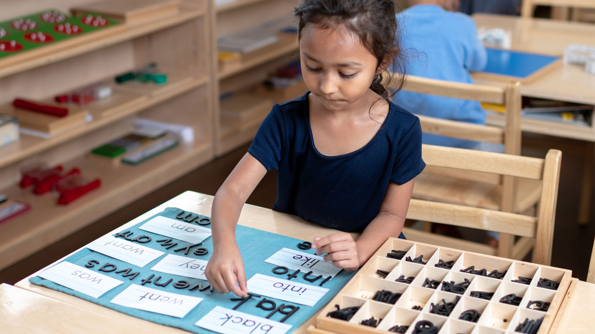 A girl sitting on a chair and learning how to spell with flashcards and toy letters